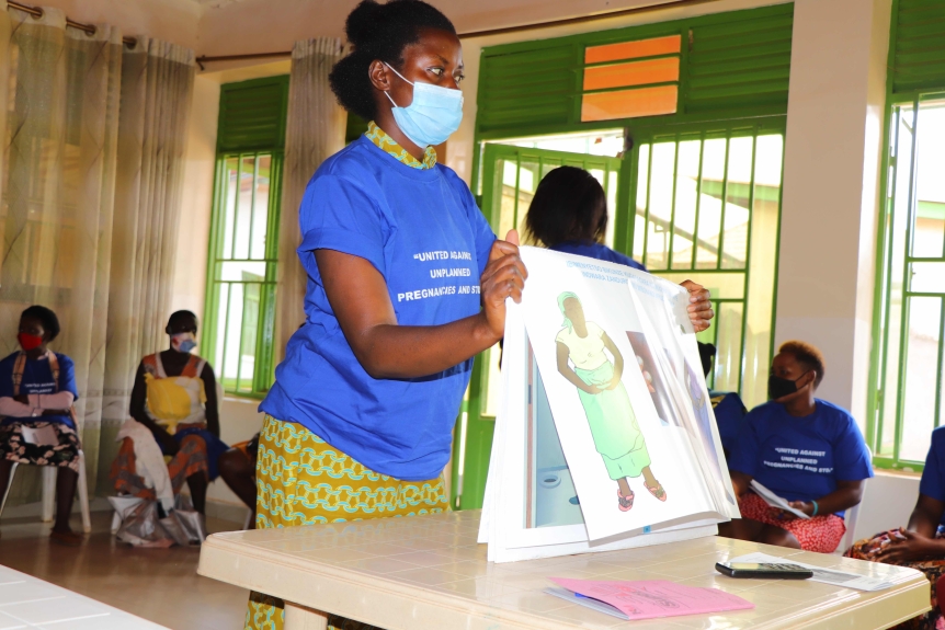 A woman in a mask and blue t-shirt with the text "United Against Unplanned Pregnancy and STDs" in white flips to a new page in an oversized picture book