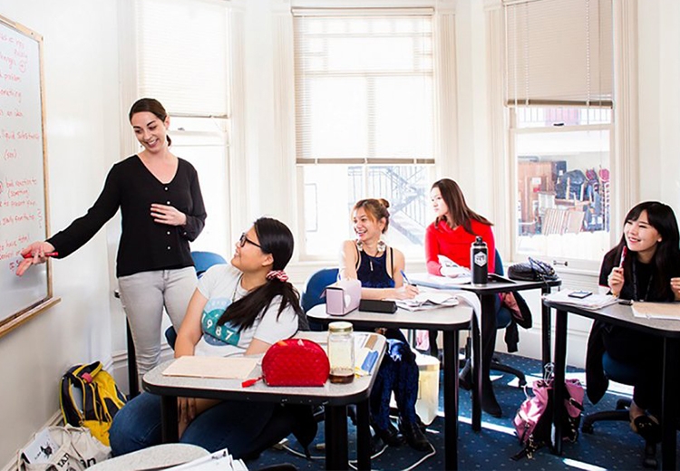 Teacher gesturing towards whiteboard while students look on smiling