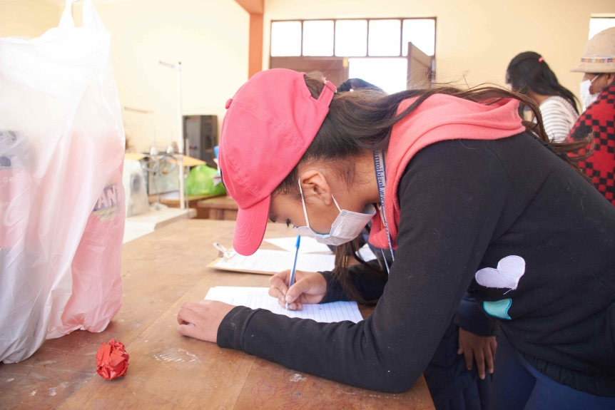 A young woman in a mask and pink hat writes on a piece of paper