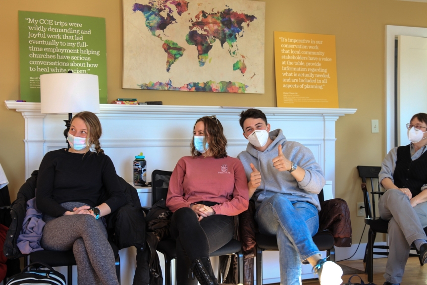 Students in the CCE Community Connected Learning course in class. One student looks at the camera with two thumbs up while the other two are listening to a speaker.