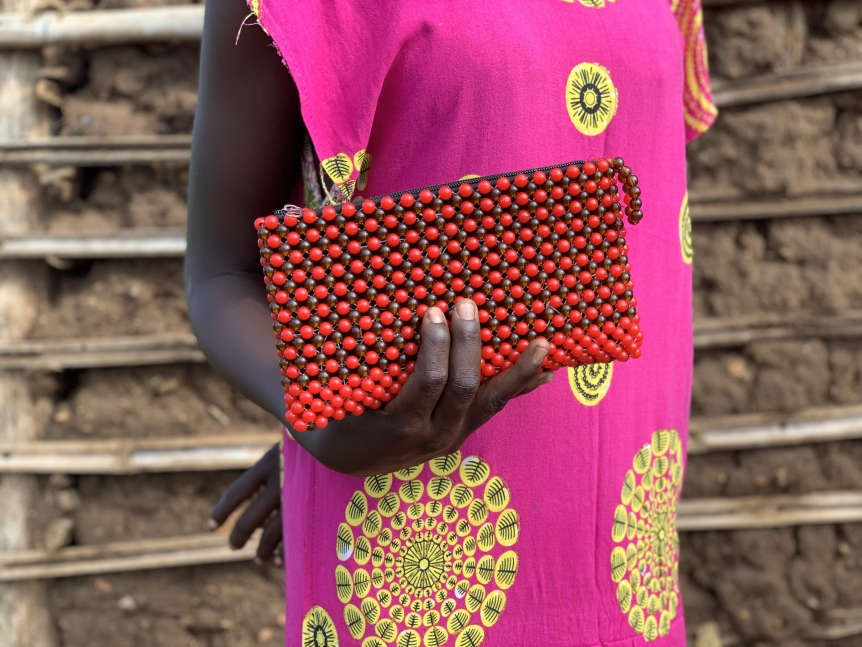 A woman's hand holds out an orange, beaded, purse.