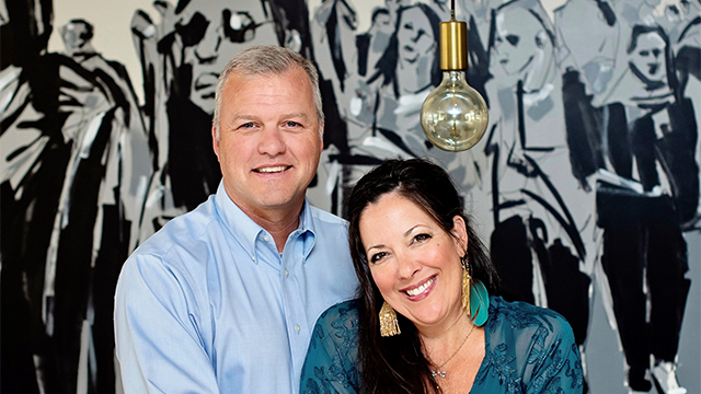 JP Watson and partner pose in front of a large black and white mural of a crowd