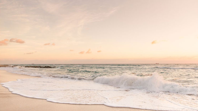 An image of waves lapping onto a quiet beach at sunrise.