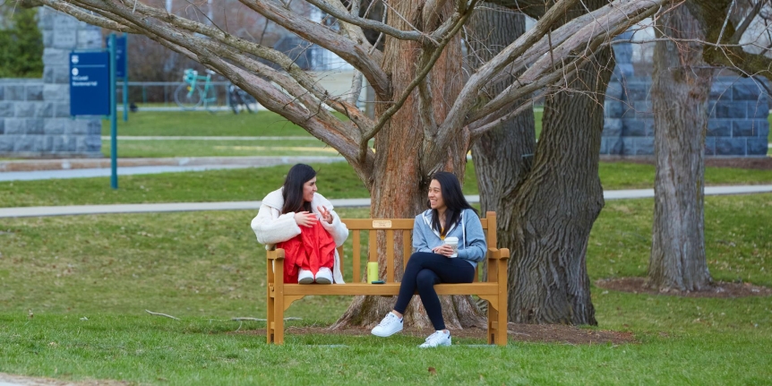 Two women sitting on a bench in fall. THey are smiling and talking.