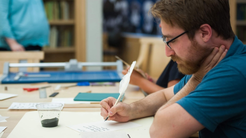 A student writes with a feather pen and ink.