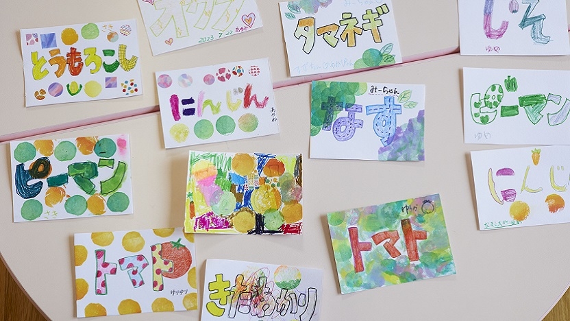 12 colorful paintings with Japanese writing sit on a white table.