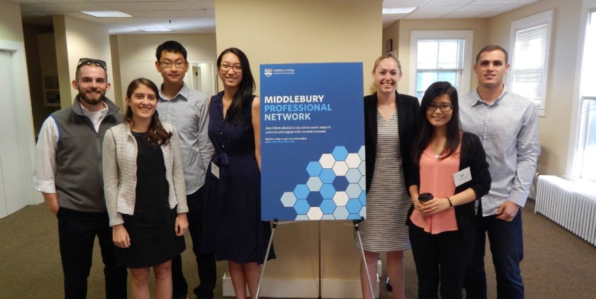 A group of 7 alumni standing with the Middlebury Professional Network sign at one of our alumni events.
