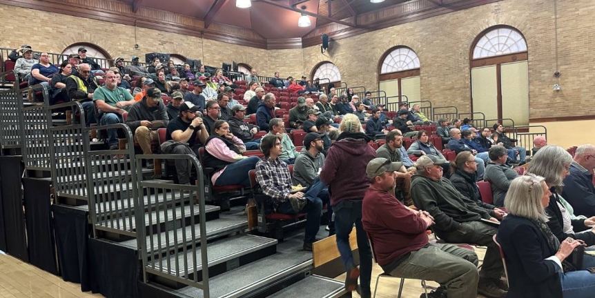 A photo of a large group of staff sitting in bleachers listening to the speakers.