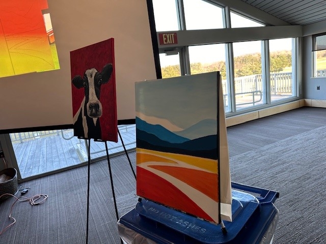 Two canvases, one of a cow and one of mountains, used as examples of final results for the paint and sip