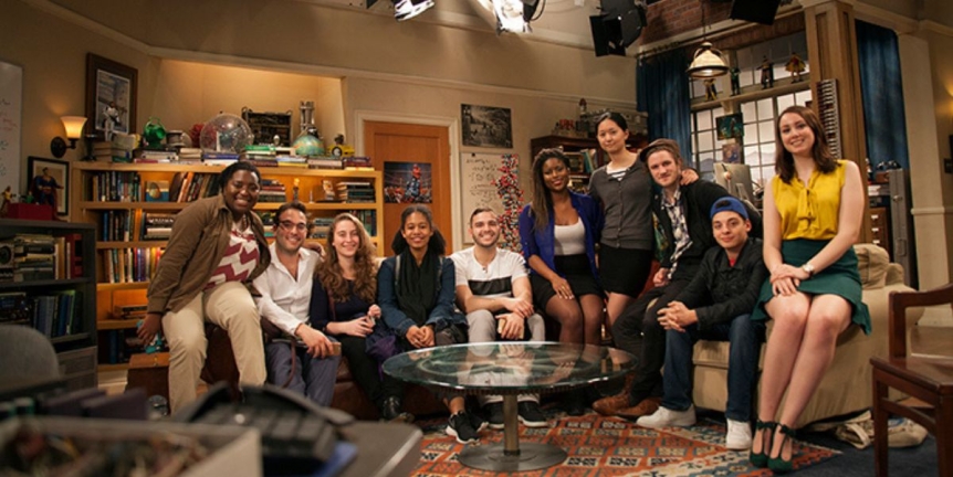 Group photo on the set of the Big Bang Theory. 10 students seated in the living room facing the camera.