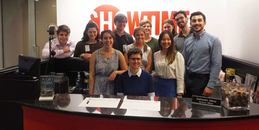 10 Middlebury students standing behind the Showtime reception desk at the Showtime headquarters in NYC.