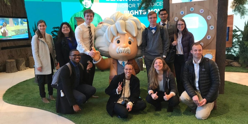 A group of students posting with the Salesforce "Einstein" statue in the lobby.