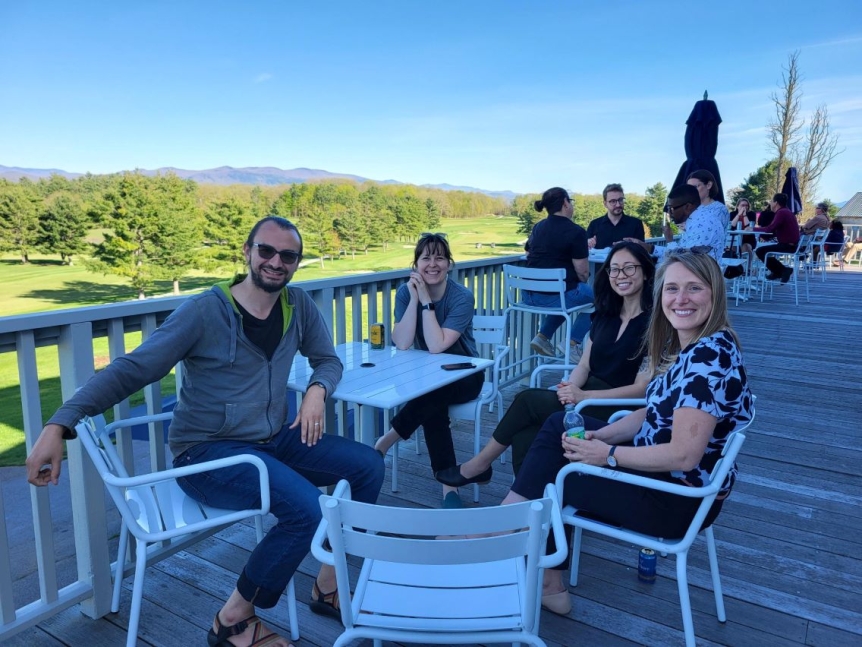 Four colleagues sitting on the porch smiling enjoying drinks.