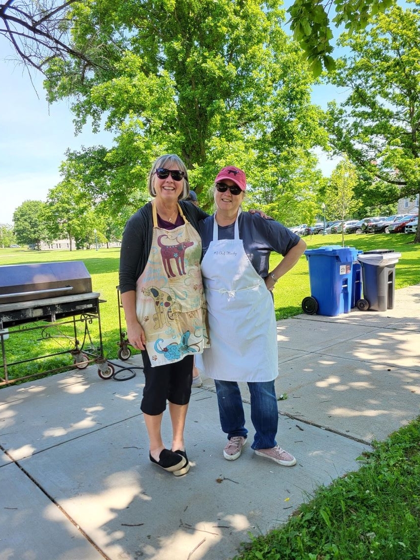 Two colleagues standing together in front of a grill wearing aprons getting ready to cook