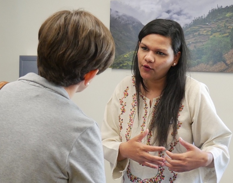 a young woman with long dark hair leans forward to speak to another person