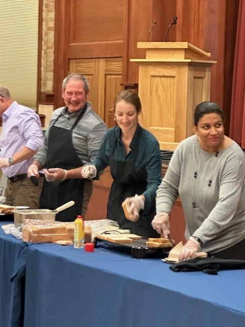 Colleagues standing together laughing making grilled cheese