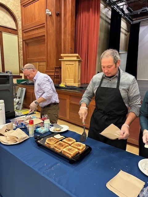 Colleagues standing together laughing making grilled cheese