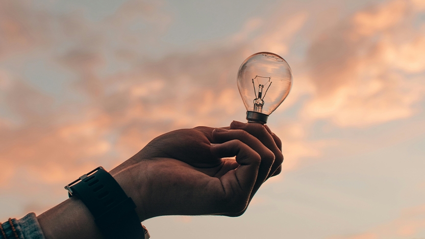 Hand holding a lightbulb with with clouds in the background
