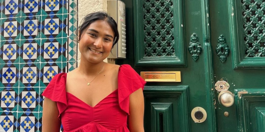 Narjis Nusaibah poses in a red dress in front of a green door and tiled wall.