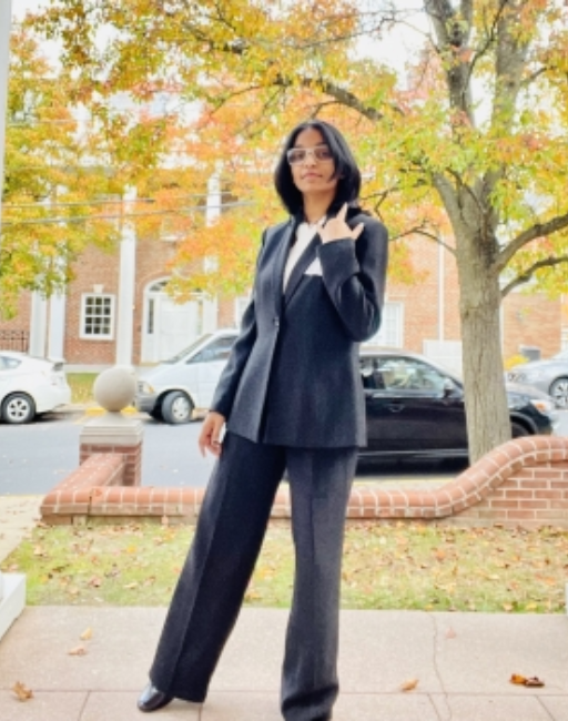 Anshika Patel wears a suit and poses outside in front of fall foliage.