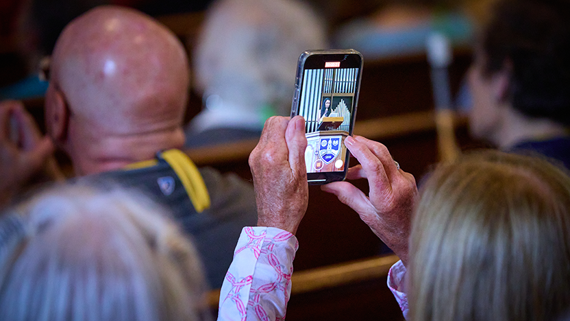 A member of the Class of 1975 holds up her phone to take a photo of the speaker at the podium during Reunion Convocation