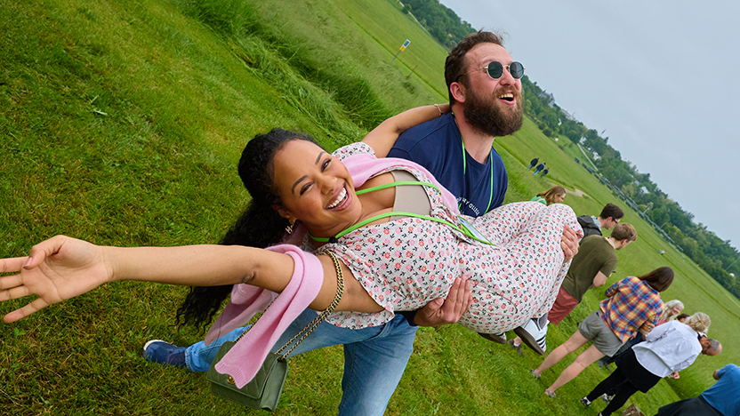 A Class of 2015 Reunion attendee smiles with an arm outstretched as though flying while being lifted in the arms of another attendee