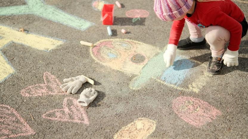 Young child writing on the sidewalk with colored chalk.