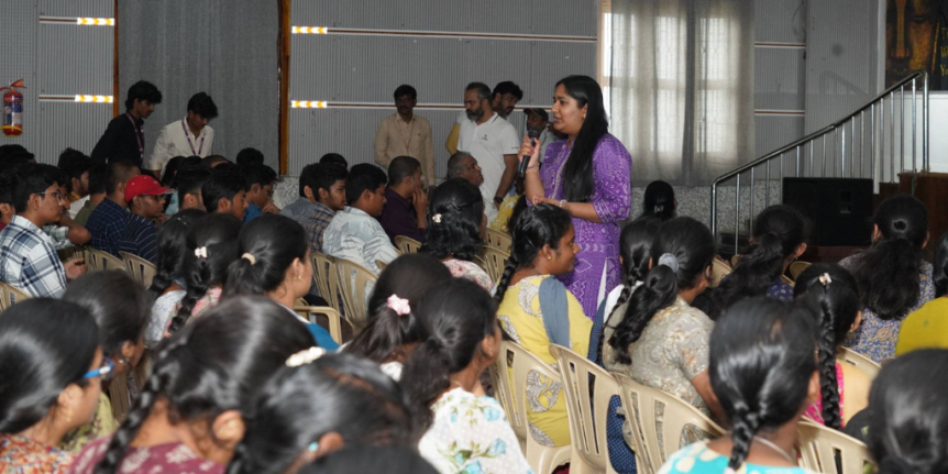 A person wearing a purple dress speaks to a room of people.