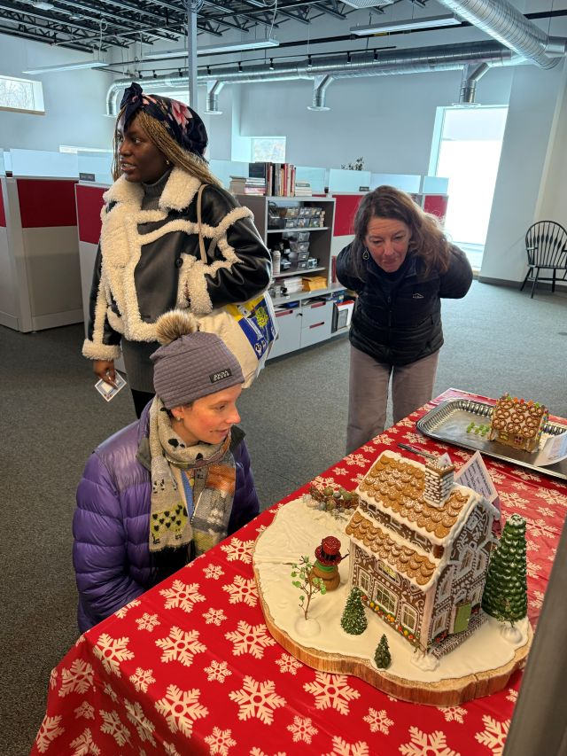 staff looking at gingerbread house on red table