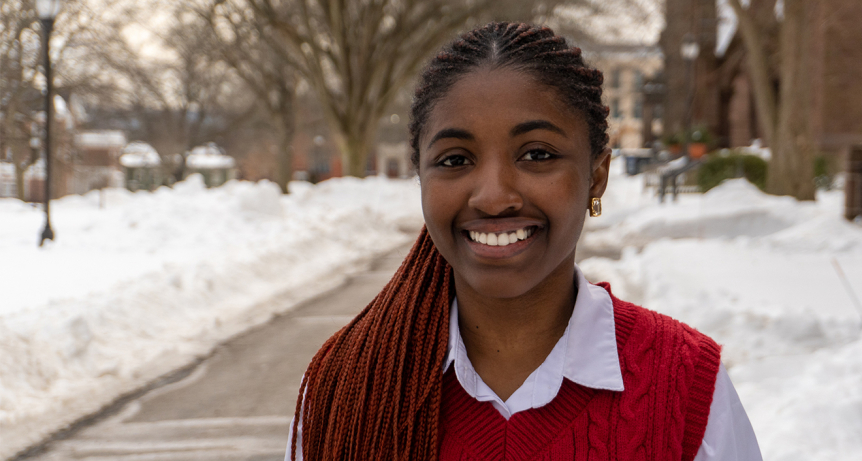 A person looks at the camera with a smile. It's winter, there is snow behind them, but it doesn't seem cold.
