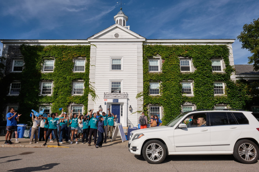 Student staff cheer as a family drives up to a building
