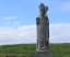 stone sculpture of St. Patrick standing in green field against blue sky