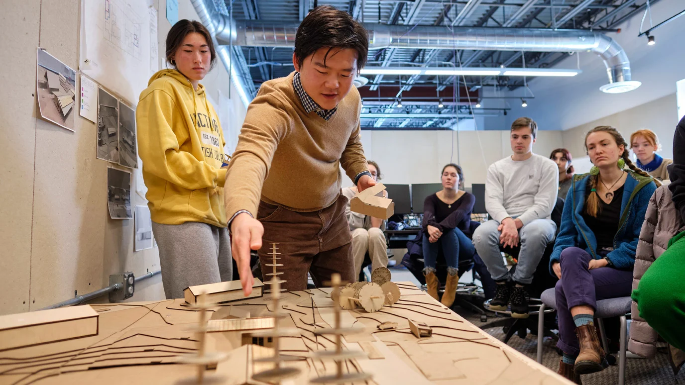 Students observe a presentation that utilizes a cardboard model.