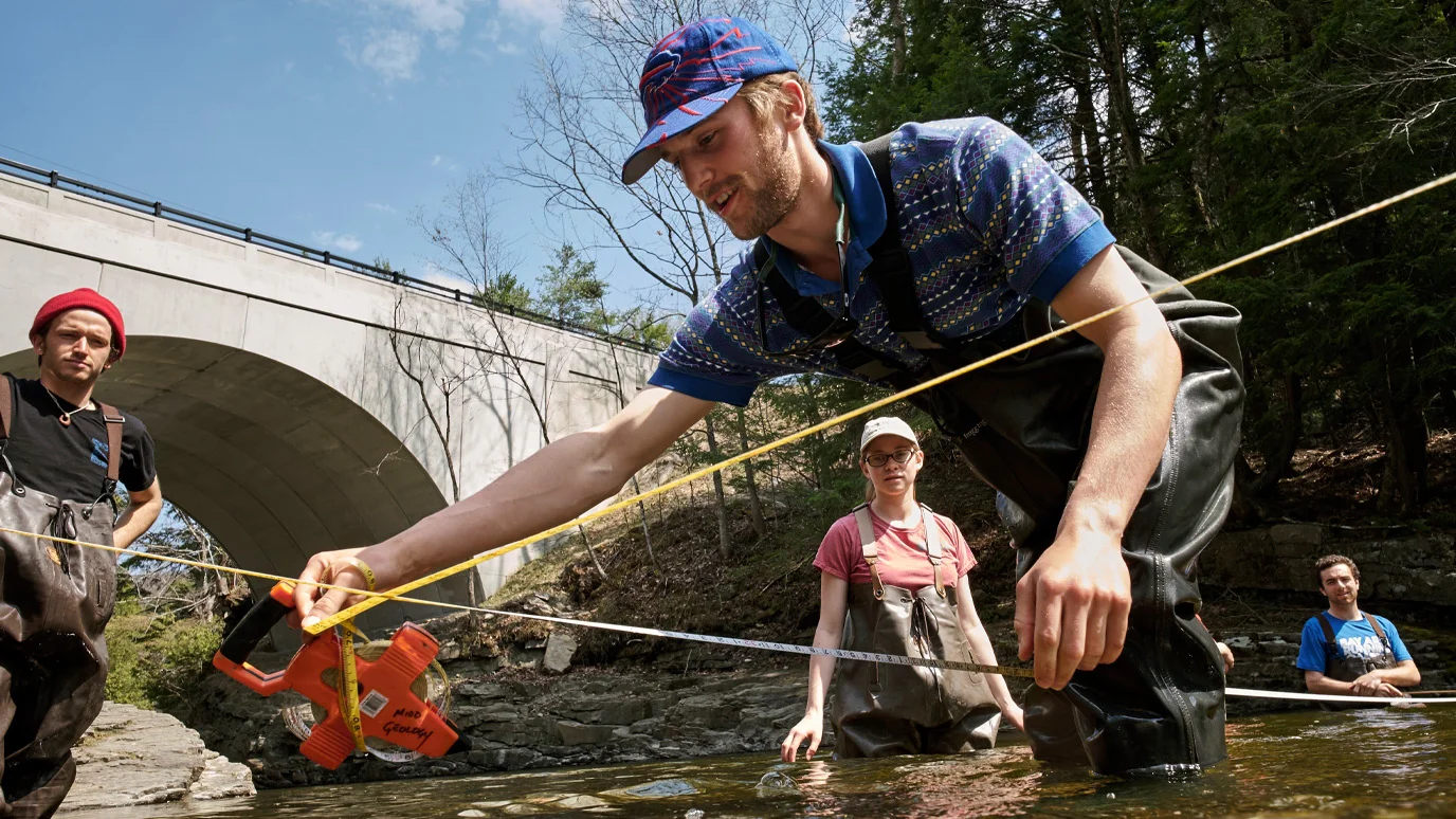 People in waders take measurements in a stream under a bridge.