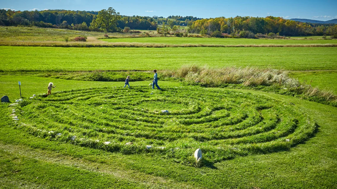A woman and two small children walk amongst the stone circluar maze at the Knoll.