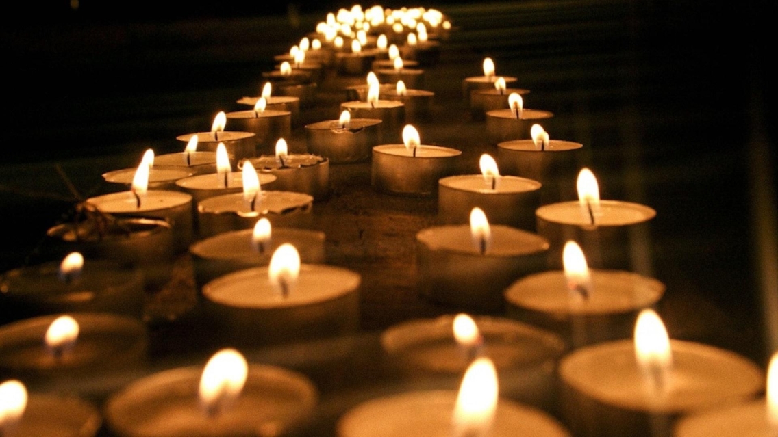 long grouping of lit candles against a dark backgr9und