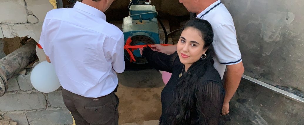 Amina Fatkhulloeva looks back at the camera and smiles in front of a new water pump