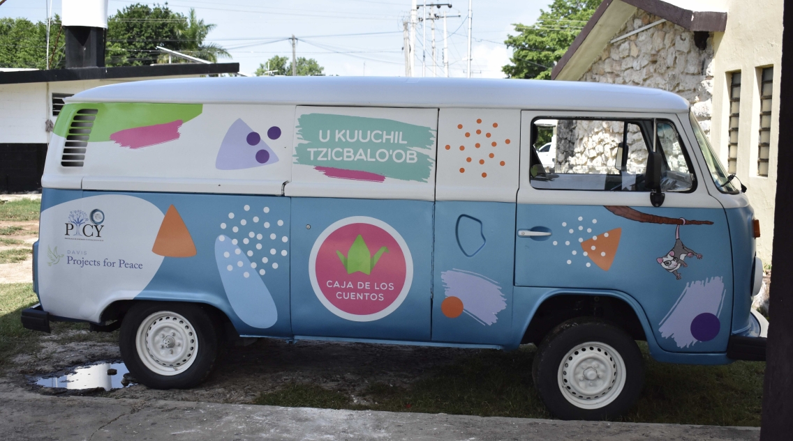 A colorfully painted Volkswagen van covered in blues, whites, and pinks.
