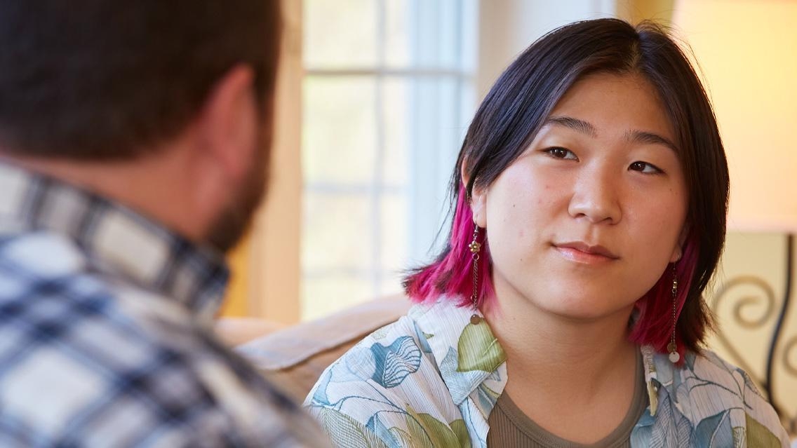 Framed over-the-shoulder of her interviewer, Cassia Park listens to question, wearing a patterned short-sleeve shirt.