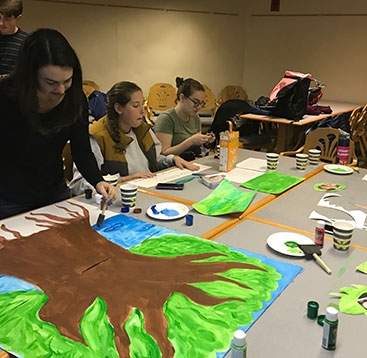 Three students painting a tree on a large piece of paper.