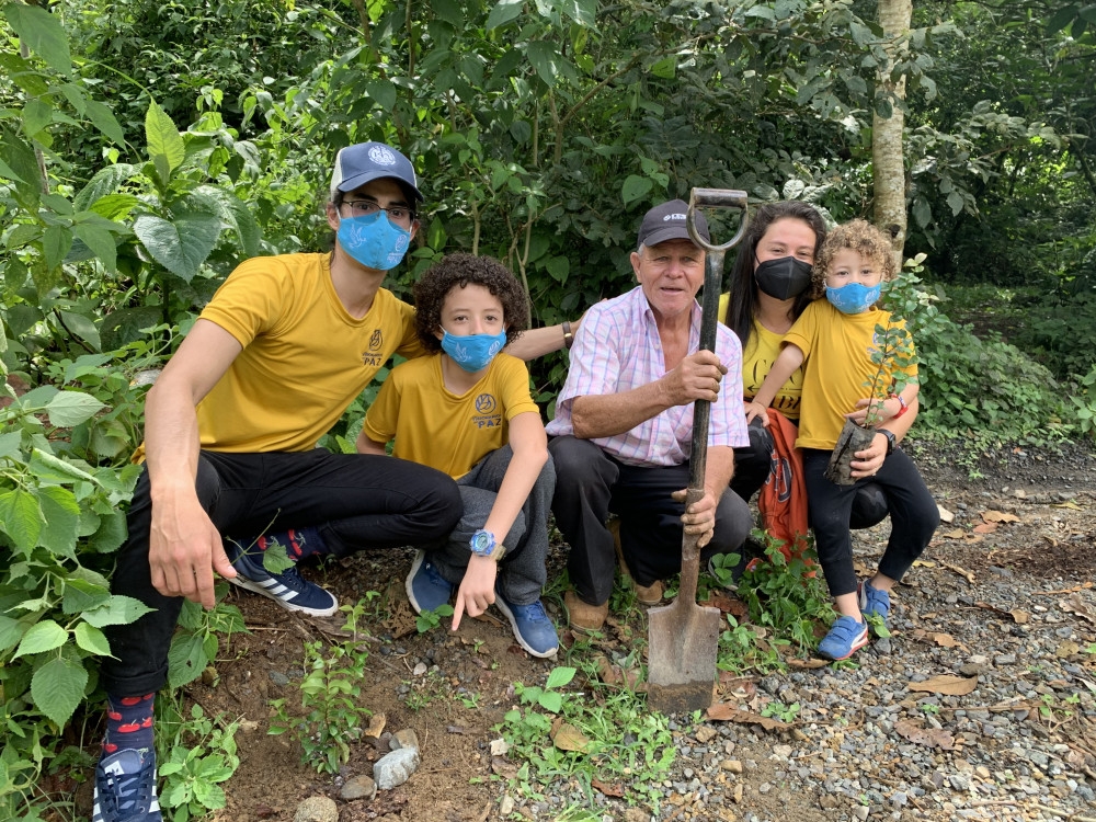 Mauro José Ramírez Azofeifa​​​​​​​, wearing a yellow shirt, black pants, ball cap, and surgical mask, poses with three children and their parents.