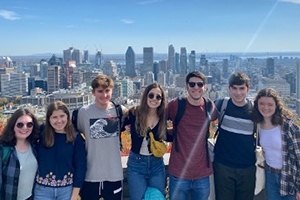 Seven students stand in front of skyline.
