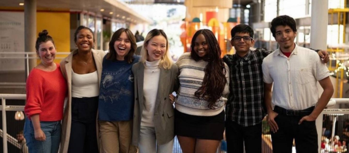 A group of seven students standing arm in arm and smiling at the camera.