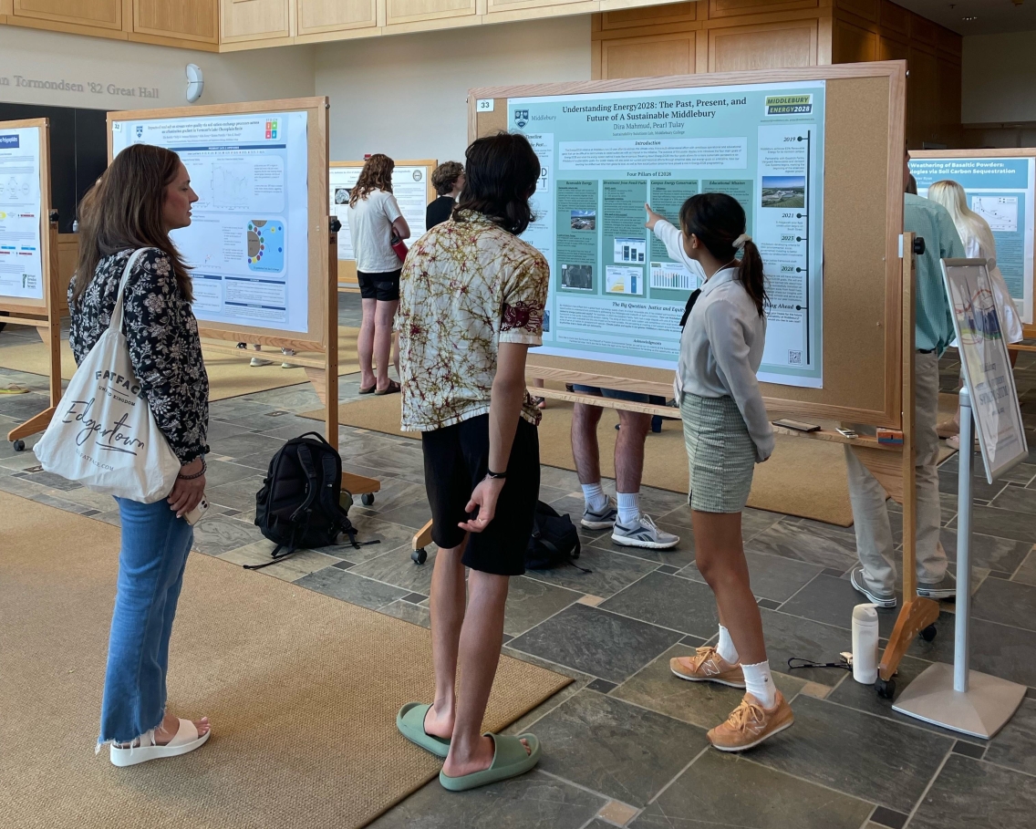 Student Dira Mahmud talking with two individuals who are interestedly looking at her large Energy 2028 poster presentation.