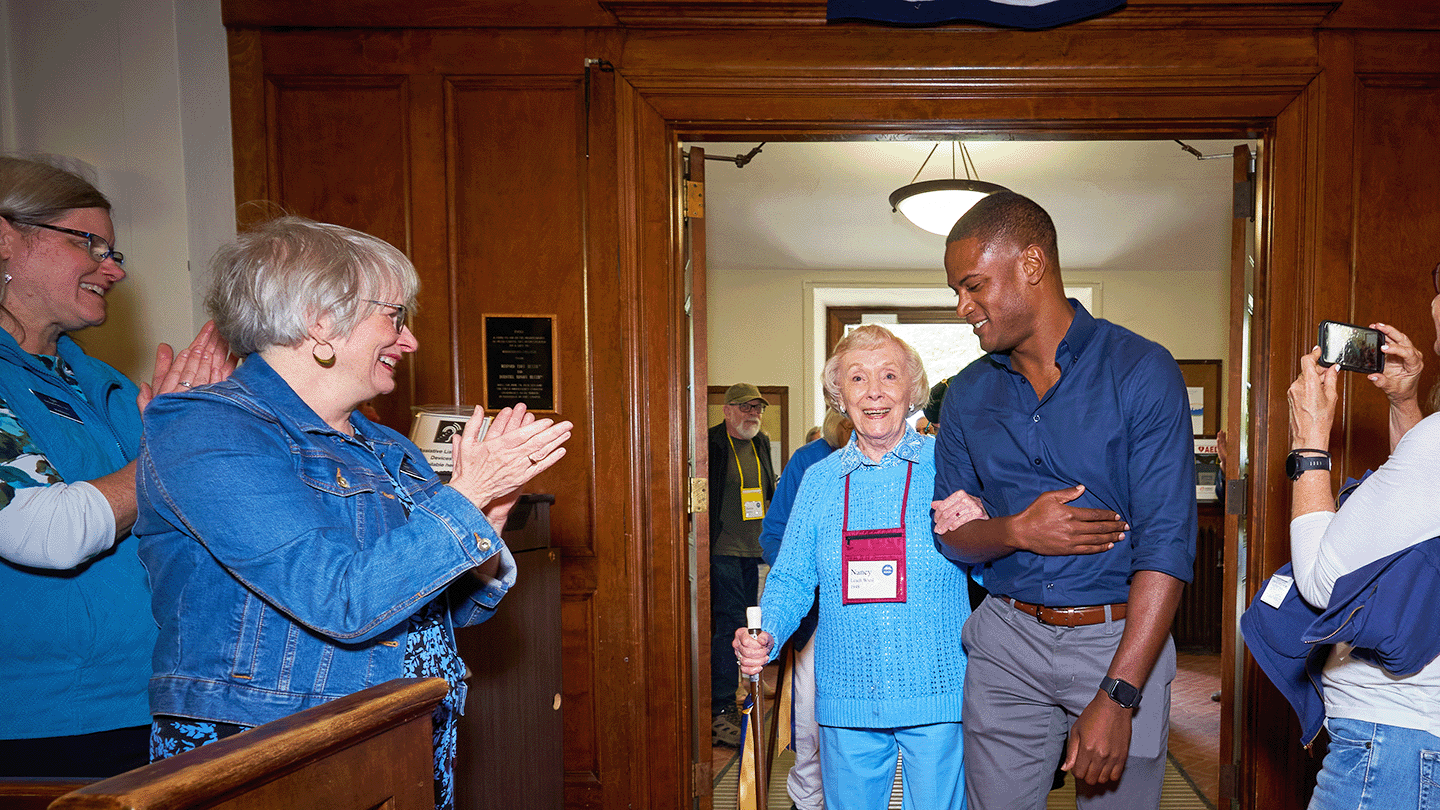 Alumni association president David Ellis ’09 escorts Nancy Leach Ward ’48 into the college chapel at Reunion Convocation, as other alumni and staff stand to applaud.