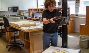 A young woman in jeans and a black t-shirt is working on photographing a piece of art at the Shelburne Museum.