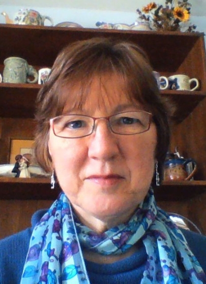 Close up of JoAnn Brewer in a blue scarf in front of a shelf of tea cups.