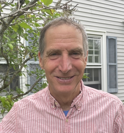 smiling man standing outside beside a house and tree