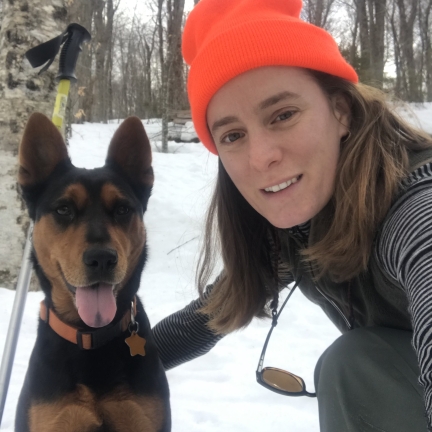 Woman wearing orange hat, crouching with dog on a snowy day