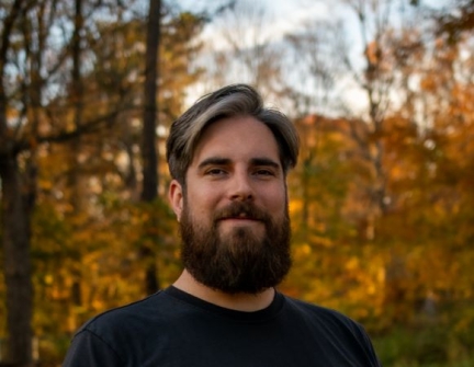 Smiling man with beard in front of Fall foliage